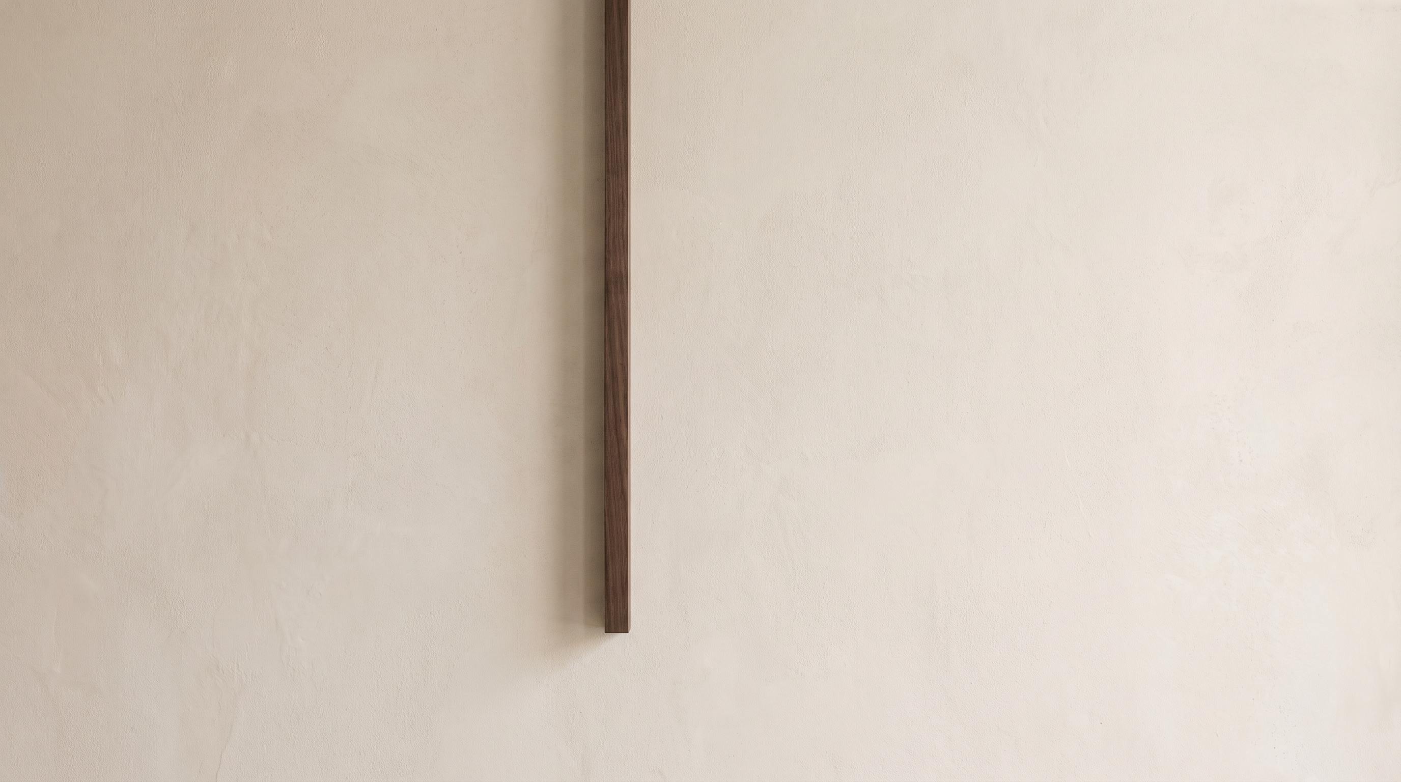 Abstract composition with one tidy dark line descending against soft plaster